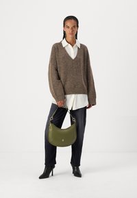 Brun strikket genser med V-hals, hvit skjorte under, mørke jeans, svarte hælboots og en grønn skinnveske.