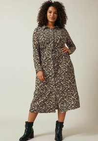 Langes, knöpfbares Kleid mit einem schwarz-beigen Zickzackmuster, tailliertem Bund und langen Ärmeln. Dazu schwarze Stiefeletten.