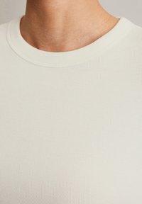 Krämfärgad, ribbad stickad t-shirt med rundad halslinning. Tyget ser slätt ut och är något elastiskt. Minimalistisk design, inga synliga mönster.