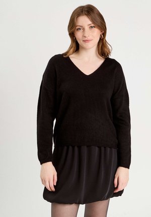 Schwarzer, gestrickter Pullover mit V-Ausschnitt und überschnittenen Schultern, mit einem lockeren Schnitt und geripptem Saum, kombiniert mit einem schwarzen Kleid.