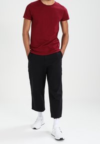 Camiseta de algodón burdeos con mangas cortas y un bolsillo en el pecho, combinada con pantalones recortados negros y zapatillas blancas.