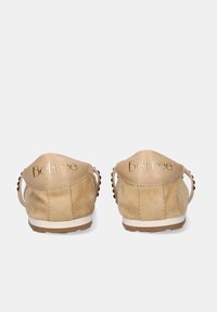 Zapatos beige de ante sin cordones con la inscripción "BeFree" en letras doradas en los talones, costuras visibles y suelas de goma blanca, mostrados desde atrás.