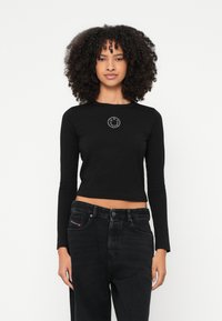 Čierny krátky top s dlhým rukávom a okrúhlym výstrihom, zdobený logom usmievajúcej sa tváre v bielej farbe. Kombinovaný s čiernymi džínsami s vysokým pásom.