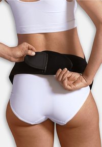 Musta tukivyö kiinnitetään vyötärön ympärille, jossa on sileä rakenne ja säädettävät ominaisuudet, käytetty valkoisen crop topin ja alushousujen päällä.