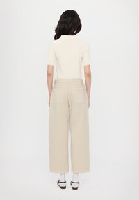 Beige wide-leg trousers made of cotton, with two back pockets, paired with a short-sleeve, cream-colored top.