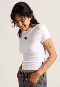 Top bianco a maniche corte con costine e design aderente, caratterizzato da un logo nero "VANS" sul petto. Tessuto testurizzato e lunghezza corta.