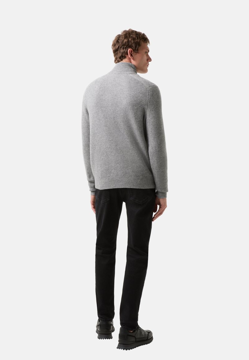 Grau gerippter Strickpullover mit hohem Kragen, getragen mit schwarzen Jeans und dunklen Schuhen, von hinten betrachtet. Die Textur ist weich und warm.