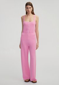 Roze gebreide jumpsuit met wijde benen, mouwloos ontwerp, knopen aan de voorkant en gestructureerde stof. Minimalistische stijl zonder zichtbare patronen of accenten.