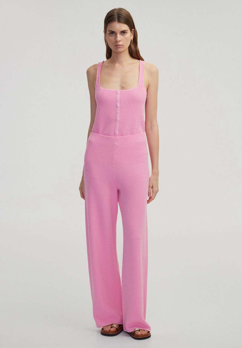 Roze gebreide jumpsuit met wijde benen, mouwloos ontwerp, knopen aan de voorkant en gestructureerde stof. Minimalistische stijl zonder zichtbare patronen of accenten.