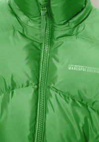 Green puffer jacket with a high collar, smooth, shiny texture, front zipper, and branded accents. Features stitched sections for insulation.