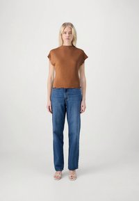 Rjav top z kratkimi rokavi z teksturirano površino, kombiniran z modrimi kavbojkami z ravnimi hlačnicami. Top ima valovit rob in sproščen kroj.