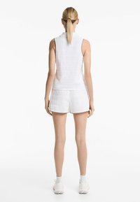 Top bianco senza maniche in stile polo con tessuto testurizzato, abbinato a pantaloni corti coordinati con bordi a contrasto.