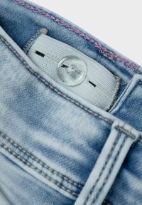 Jeans de mezclilla azul claro con un acento de costura rosa, que cuentan con un botón redondo transparente y una etiqueta tejida visible en la cinturilla.