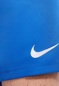 Shorts de sport bleus en tissu texturé. Présentent un logo Nike brodé en blanc en bas à gauche et des coutures soignées le long de l'ourlet.