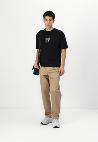 Sort bomulds t-shirt med hvid grafisk tekst, parret med beige bukser og grå sneakers. Minimalistisk design med en afslappet pasform.