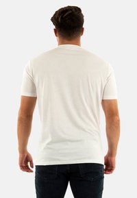 T-shirt bianco a maniche corte realizzato in tessuto morbido, con scollo rotondo e vestibilità rilassata. Il modello indossa jeans scuri.