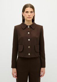 Brun cropped jakke med rund krave, sølvknapper og to forlommer. Glat tekstur og skræddersyet design.
