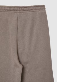 Pantaloni in cotone marroni con una cintura elastica, caratterizzati da una texture morbida e liscia e un design semplice e rilassato. Nessun motivo o dettaglio visibile.