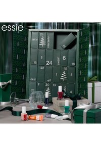 Un calendrier de l'Avent vert avec des portes numérotées, contenant divers flacons de vernis à ongles dans des couleurs comme le rouge, le bleu-vert et le rose. Comprend des boîtes décoratives et un ruban.