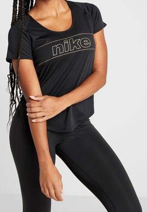 Vrouw draagt een zwarte Nike T-shirt met korte mouwen en zwarte leggings, met ingevlochten haar en één arm over haar torso gekruist.