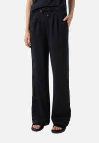 Zwarte wijde broek van zacht materiaal, met een trekkoord in de taille, zijzakken en een gladde textuur.