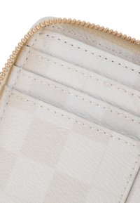 Interno di un portafoglio bianco antiritaglio RFID con tre scomparti per carte, texture in pelle liscia e dettagli con zip dorati. Branding discreto visibile.