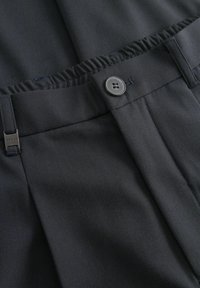 Fekete nadrág közelről, bemutatva a begombolt derékrészt, az övbújtatót fémtaggal, valamint a rugalmas hátsó paneleket az állítható illeszkedés érdekében.