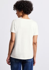 Hvid bomulds T-shirt med korte ærmer og rund hals, der har en afslappet pasform og en glat overflade. Bagview, iført blå jeans.