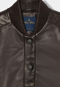 Giubbotto bomber in pelle marrone scuro con colletto a coste, chiusura frontale a scatto e etichetta interna con sfondo blu e scritte dorate.