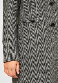 Abrigo con patrón de pata de gallo en blanco y negro. Cuenta con un solo botón, bolsillo lateral y diseño estructurado. Fabricado con tela texturizada.
