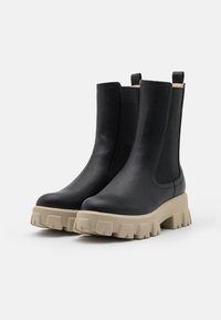 Botas de cuero negro hasta el tobillo con paneles laterales elásticos, suela de goma gruesa beige y textura suave. Cuenta con una lengüeta en la parte trasera.