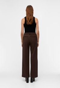 Pantalon marron à jambes larges avec taille élastique et deux poches arrière, accompagné d'un haut noir sans manches. Tissu lisse avec un léger brillant.