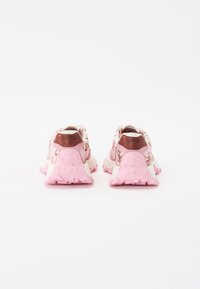 Pink shoes with a textured sole, featuring an embroidered design, contrasting white accents, and a brown heel tab with the brand name.