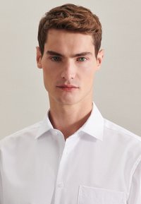 Witte overhemden met een puntkraag en een borstzak; gemaakt van zachte stof, met een getailleerde pasvorm en scherpe lijnen.