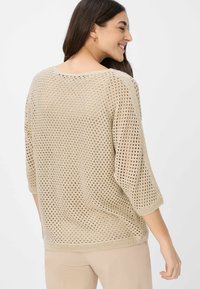 Beige gebreide trui met een losse, open structuur en driekwart mouwen, met een ronde halslijn en een geribbelde zoomafwerking.