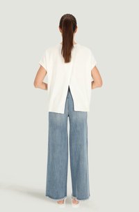 Biała bluzka z krótkim rękawem i rozcięciem z tyłu, zestawiona z jasnoniebieskimi, szerokimi spodniami dżinsowymi i białymi trampkami, prezentowana z tyłu.