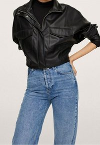 Veste courte en simili cuir noir avec deux poches avant et un col montant, associée à un jean en denim bleu taille haute.