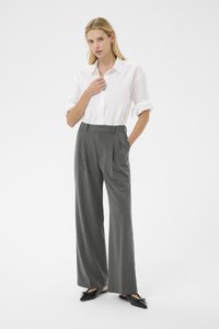 Chemise blanche à boutons avec des manches retroussées, associée à un pantalon taille haute à rayures grises. Des chaussures plates noires complètent la tenue.