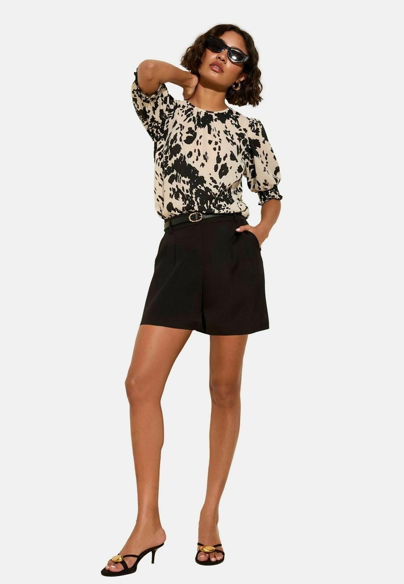 Blusa nera e panna con motivo, maniche a sbuffo, abbinata a pantaloni corti neri a vita alta e sandali neri con tacco e tocco dorato.
