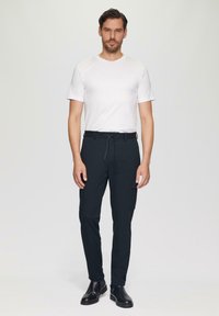 Zwarte cargo-broek met een tailleband met trekkoord en zijzakken, gecombineerd met een eenvoudig wit T-shirt en zwarte schoenen. Eenvoudig en functioneel design.