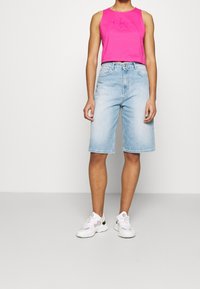 Růžový crop top na tělo, světle modré denimové bermudové šortky a bílé sportovní tenisky s černými akcenty, na jednobarevném pozadí.