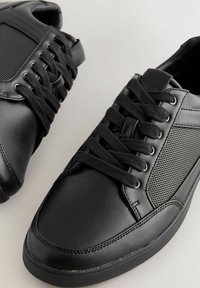 Svarta sneakers i läder och mesh med rund tå, platt snörning och texturerade sidopaneler. Syt detaljer längs kanterna.