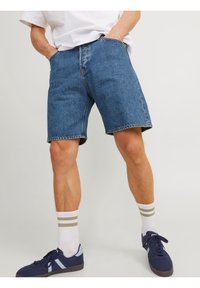 Jeansshorts i blått, med klassisk snitt, fem-fickorsdesign och kontrastsydd. Bärs med marinblå sneakers och randiga vita strumpor.
