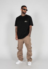 Sort kortærmet t-shirt med logo, kombineret med beige cargo bukser med sidelommer og hvide sneakers.