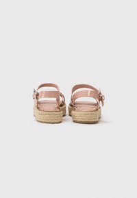 Růžové lakované espadrilky s juty platformou. Obsahují dva pásky na kotníky a detail mašle na zadní straně. Plná gumová podešev.