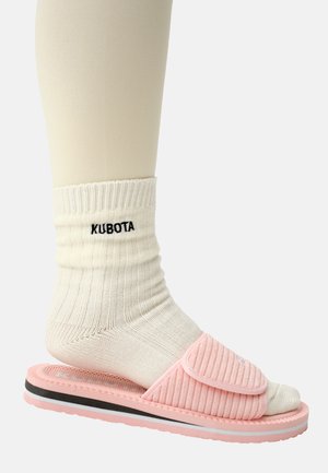 Różowe klapki z falistą cholewką, noszone na białej, falistej skarpecie; czarny logo "KUBOTA" na skarpecie. Przezroczysta podeszwa z warstwowymi kolorami.