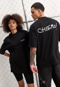 Juodos didelio dydžio marškiniai su užrašu "CHEERS!" baltu spalva nugaros pusėje. Pagaminti iš medvilnės, turi trumpas rankoves ir apvalų iškirpimą.