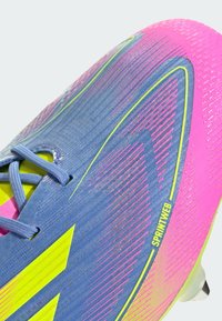 Sporting footwear with a blue upper, pink accents, yellow details, textured grip, and distinct diagonal stripes. Lace closure at the front.