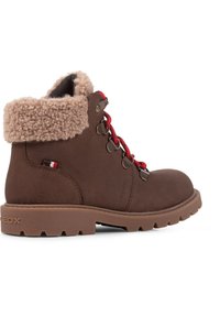 Botas de tobillo de cuero marrón con un suave cuello de piel sintética beige, cordones rojos y ojales metálicos; suela texturizada con patrones de agarre.