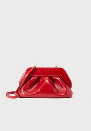 Pochette in pelle rossa con chiusura in oro, dettaglio arricciato e sottile tracolla attaccata su sfondo chiaro.